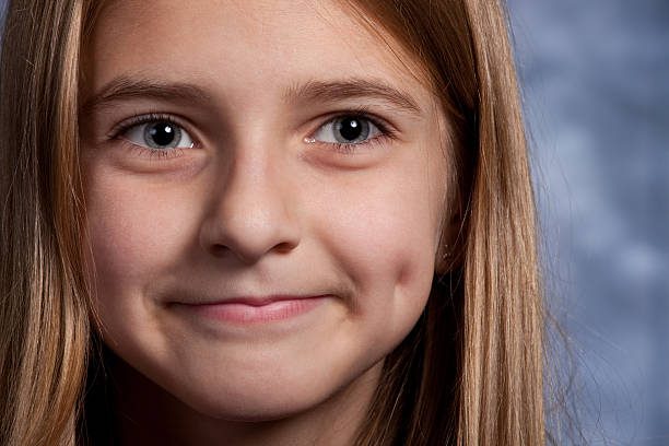 Close up photograph of a 11 year old girl smiling with a dimple. Mouth closed smile. Shadows on the face are intentional to show dimension in the childs face to enhance the expression.